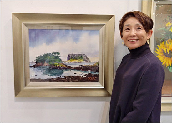제주에서 작품활동을 하는 강은희 작가가 자신의 '성산포 여름' 앞에서 환한 미소를 짓고 있다.