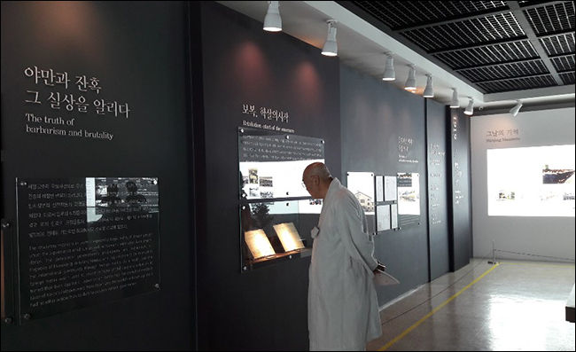전시된 사진들은 "야만과 잔혹 그 실상"을 알리고 있다. 그 사진들을 보고 있는 한 스님