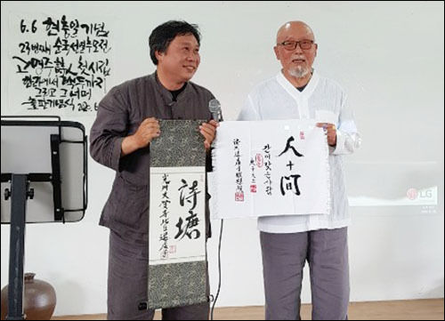 직접 쓴 ‘시당(詩塘)’이라는 아호와 '간이 맛는 사람이 되라'며 고명주 시인에게 인간(人間) 휘호를 발간 기념으로 선물하는 퇴허자 스님(오른쪽)